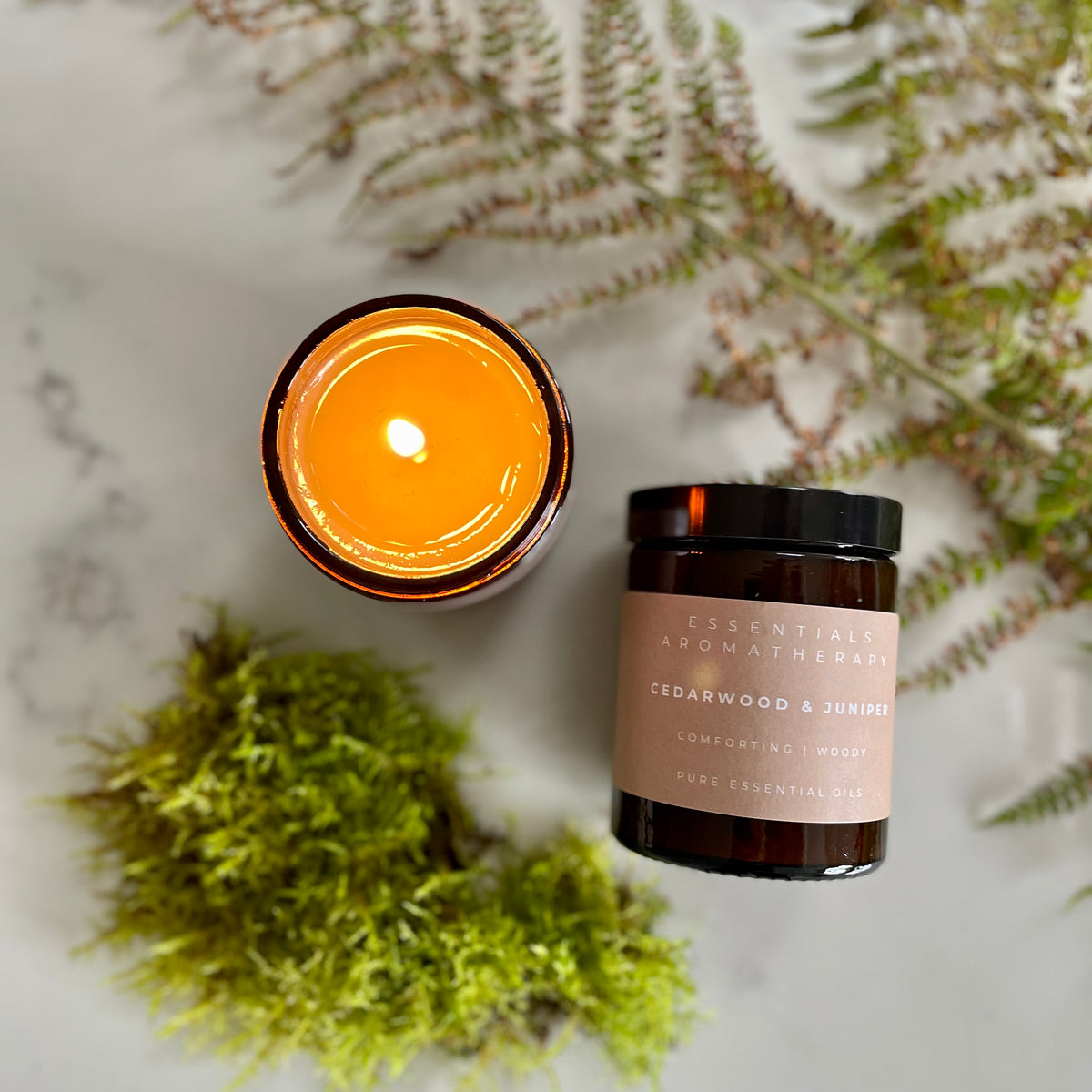 Lit Cedarwood & Juniper essential oil candle surrounded by green moss and woodland ferns.