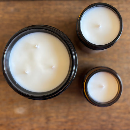 Overhead view of three unlit soy candles in amber glass jars on a wooden surface.